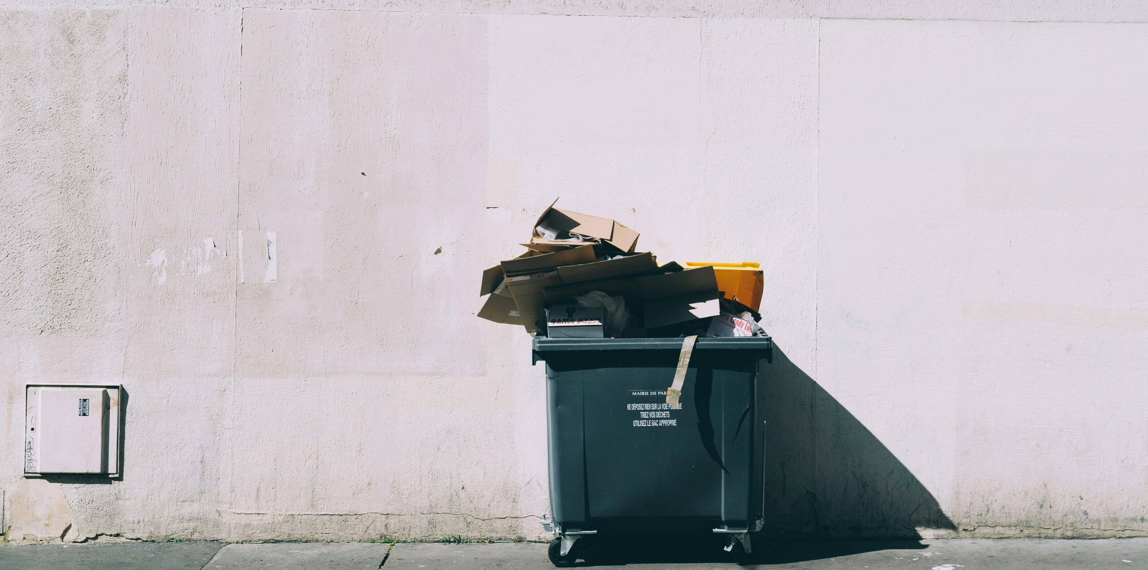 Outdoor garbage bin with cardboard waste against concrete wall